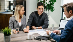 A young couple sitting across from a real estate agent holding property documents and chain of title paperwork.