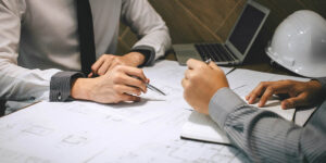 Two professionals reviewing construction blueprints and contract documents at a conference table.
