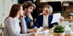 A tense couple sitting at a table discusses documents with a professional advisor during a property dispute over selling.